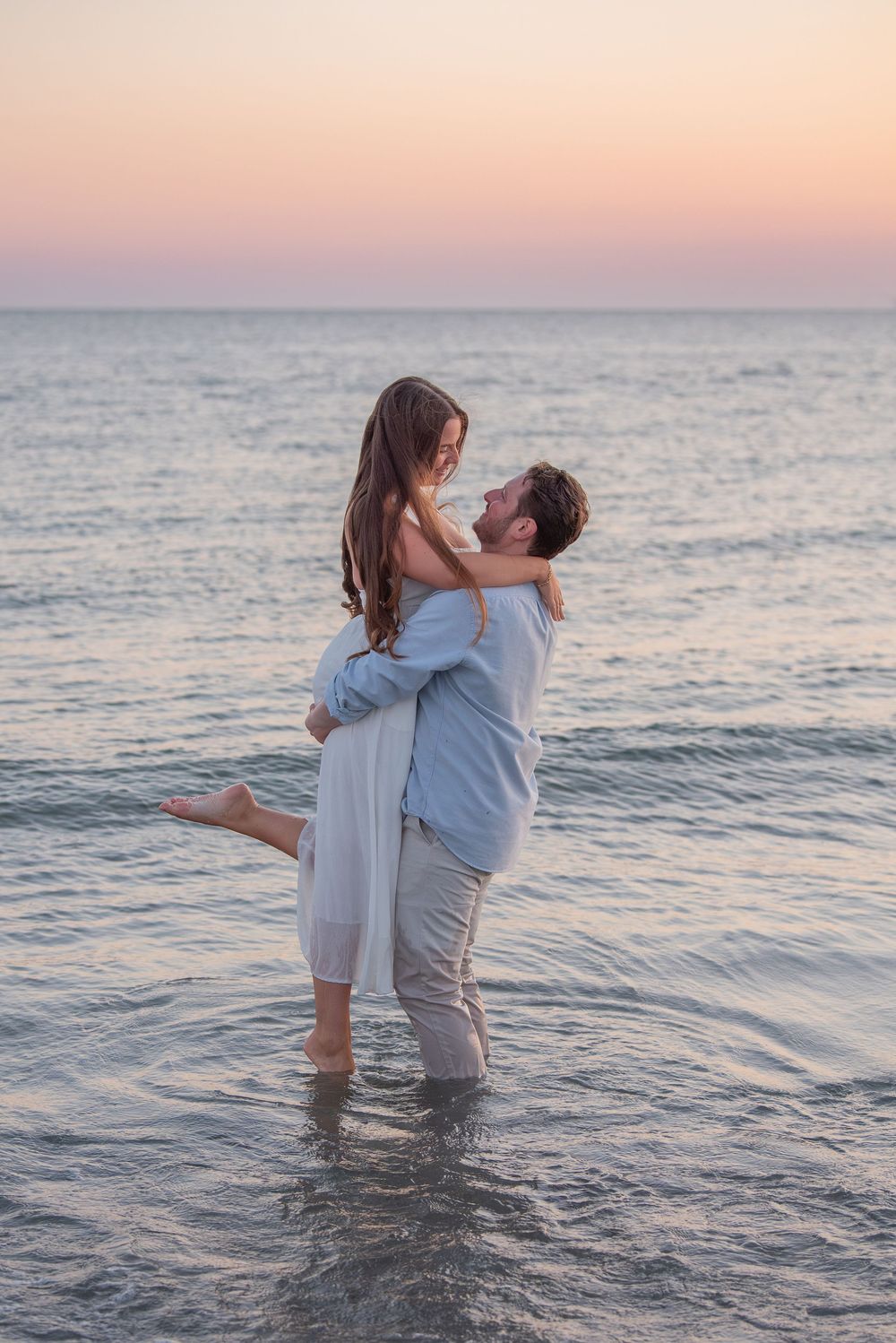 A couple plays in the ocean water during sunset creating a romantic seaside moment.