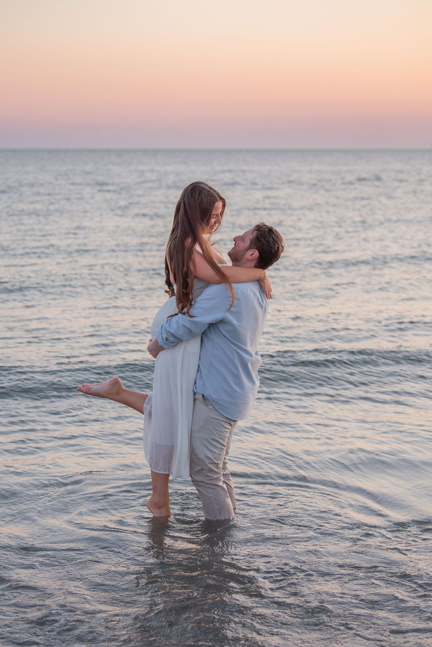 A couple plays in the ocean water during sunset creating a romantic seaside moment.