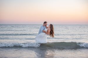 A couple splashes through ocean waves during a romantic sunset photoshoot.