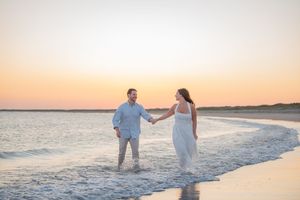 A couple walks hand in hand along the shoreline during a beautiful sunset.