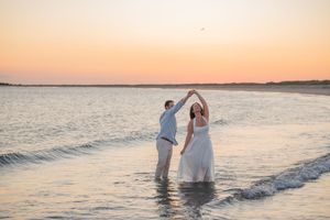 A couple dances together at the beach with the sunset creating a romantic silhouette.