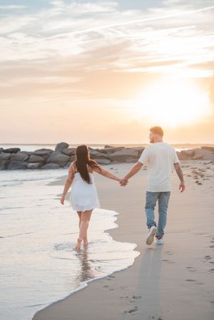 Playful couple runs along the ocean's edge at sunset, creating footprints in the wet sand.