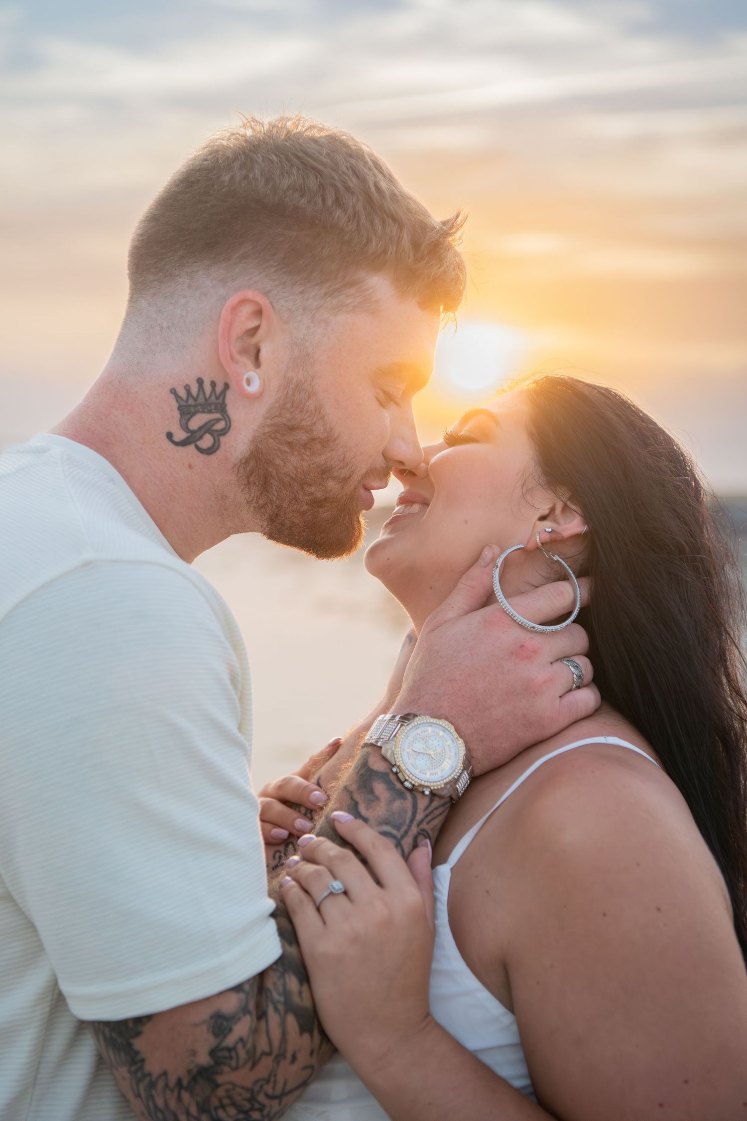 Couple shares intimate kisses during golden hour on a beach with soft sunset lighting.