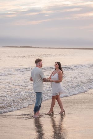 Couple plays and dances in the shallow ocean waves during sunset.