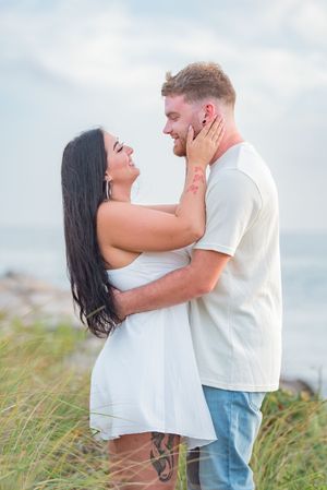 A tender moment between a couple in white outfits against a coastal backdrop.
