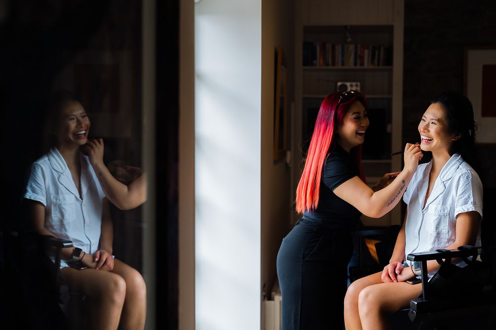 Two women getting ready in front of a mirror with beauty makeup preparations.