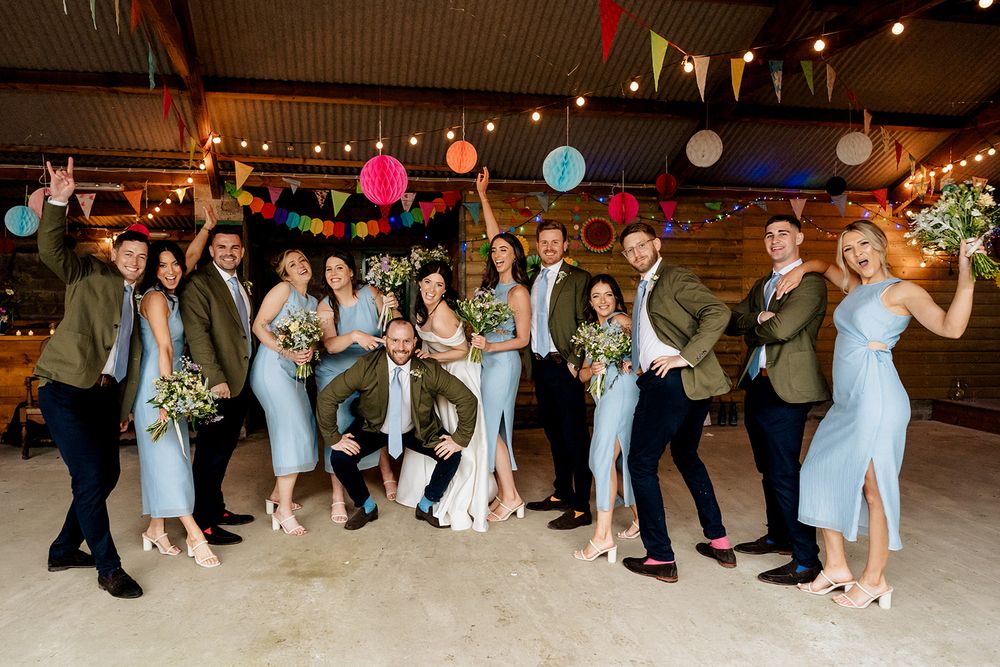 Wedding party poses together under colorful paper lanterns and decorations at indoor reception.