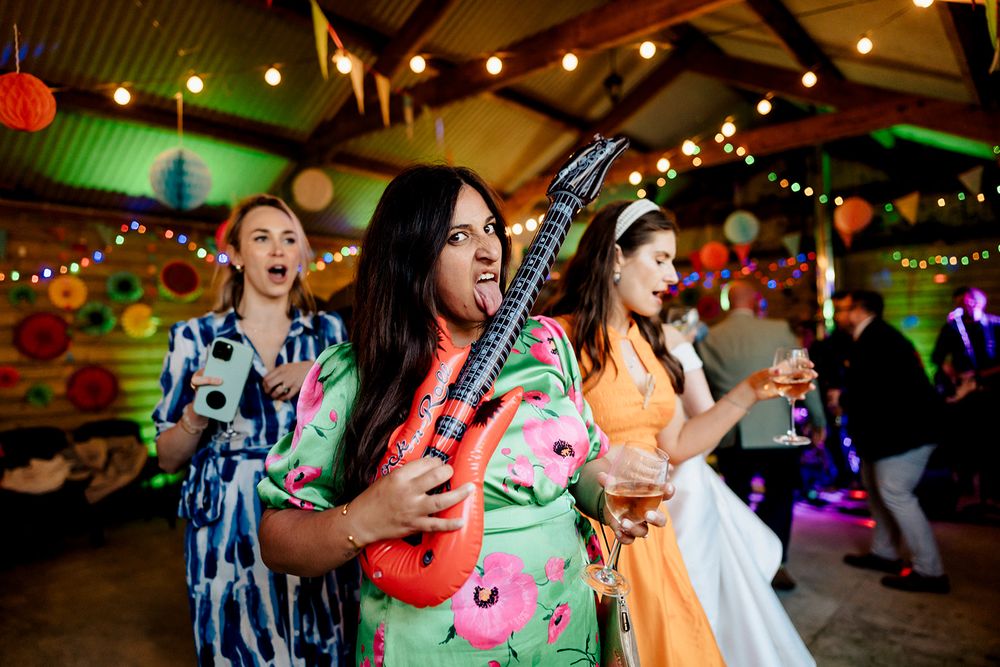 Guests celebrate at a vibrant wedding reception with colorful lighting and musical instruments.