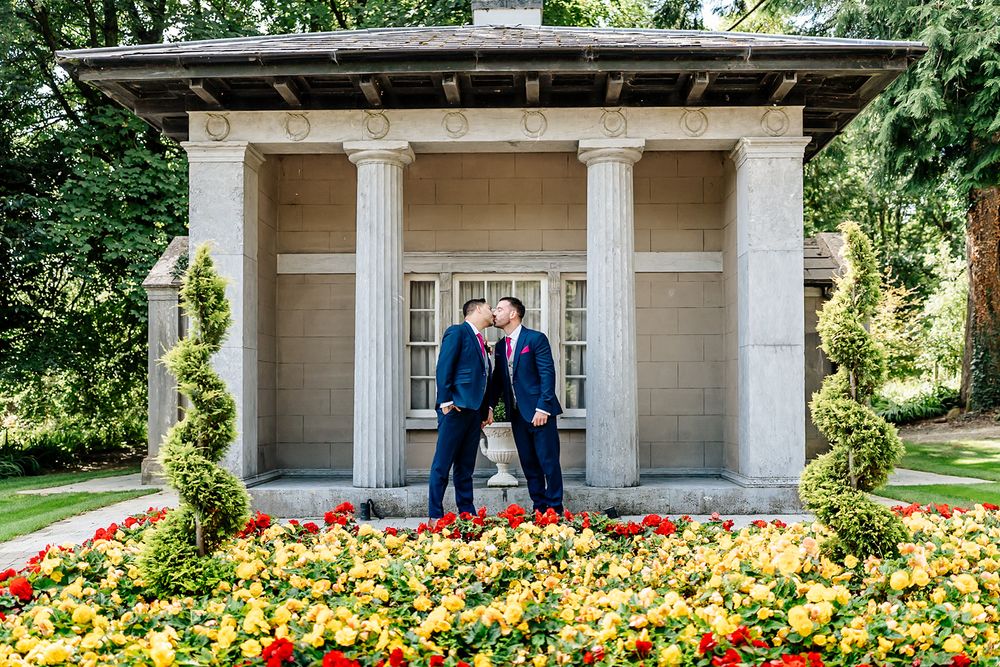 Newlyweds share an intimate moment in a garden gazebo surrounded by vibrant yellow and orange flowers.