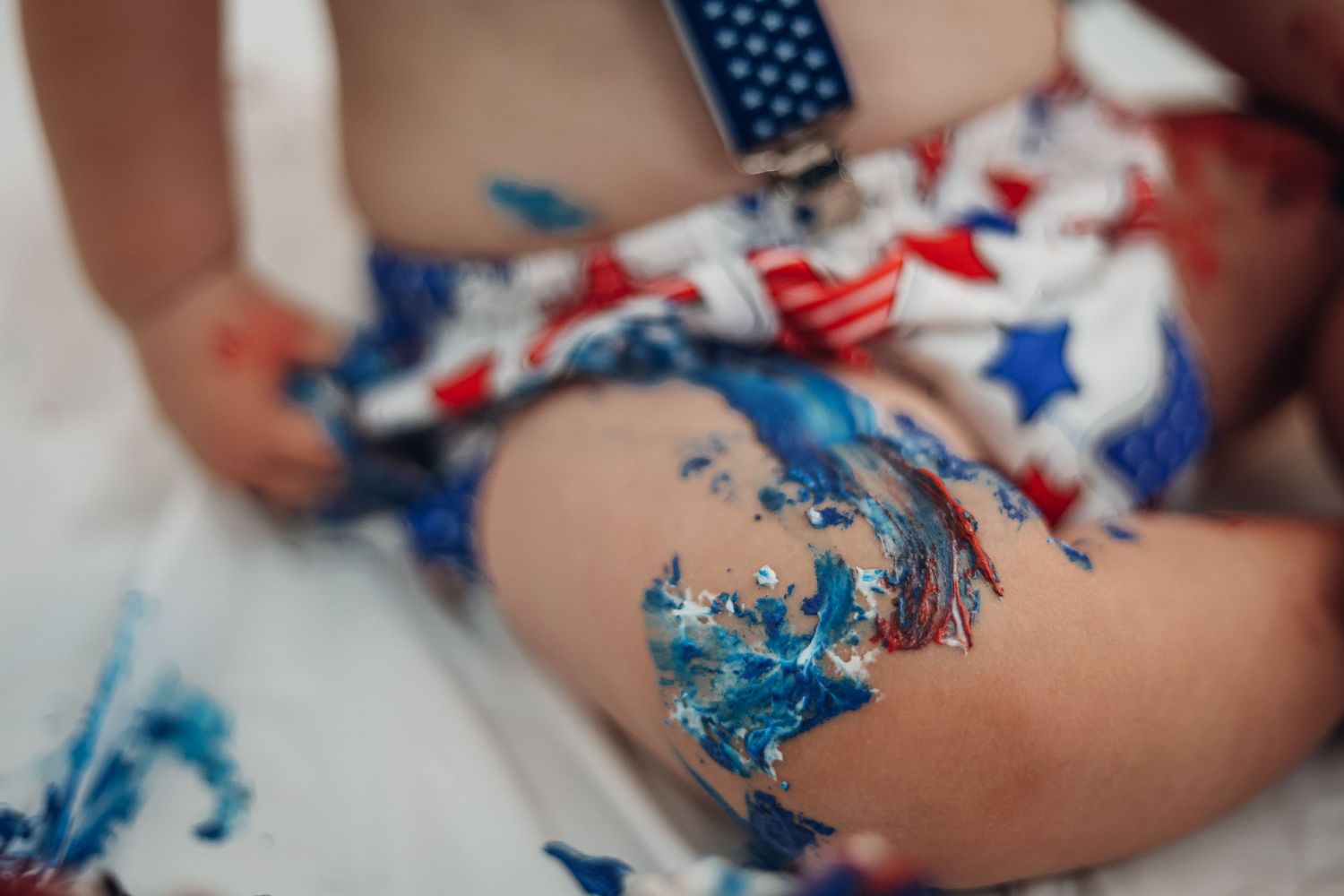 Red, white and blue frosting smeared on bare legs in a messy artistic pattern. Cake smash photography