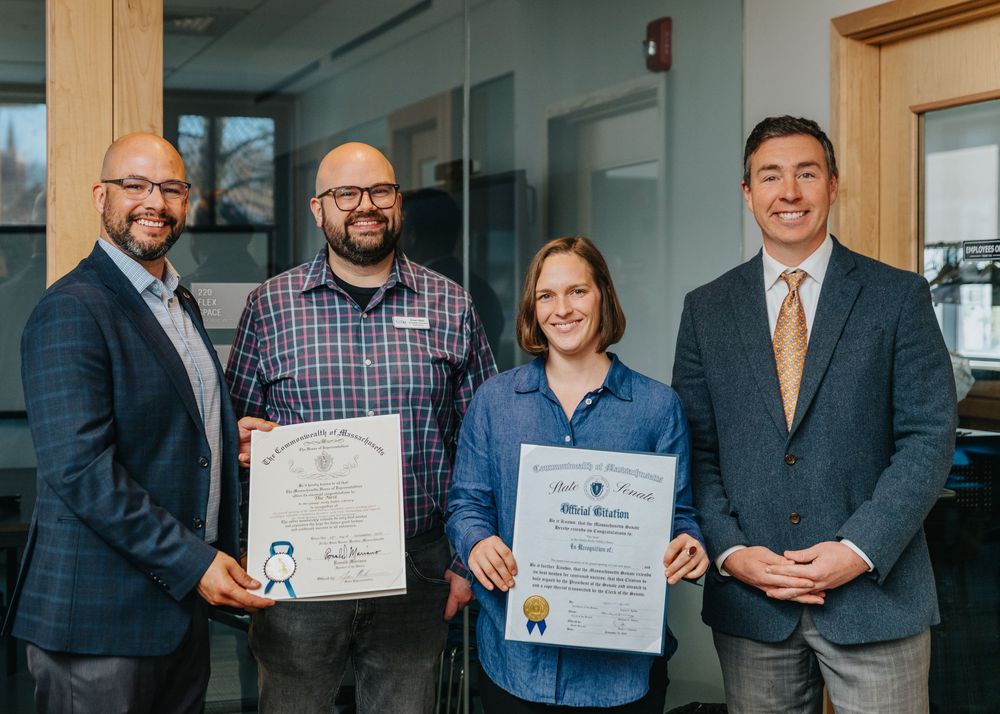 Four business professionals posing together and displaying award certificates in an office hallway.