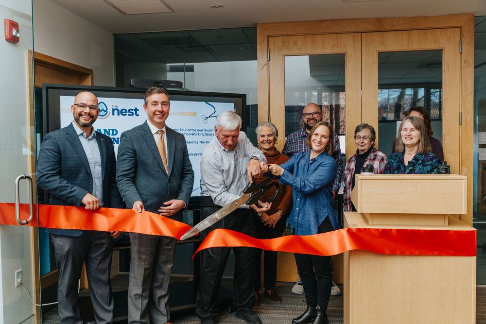 A group performing a ceremonial ribbon cutting with orange and red ribbon at a business opening event.