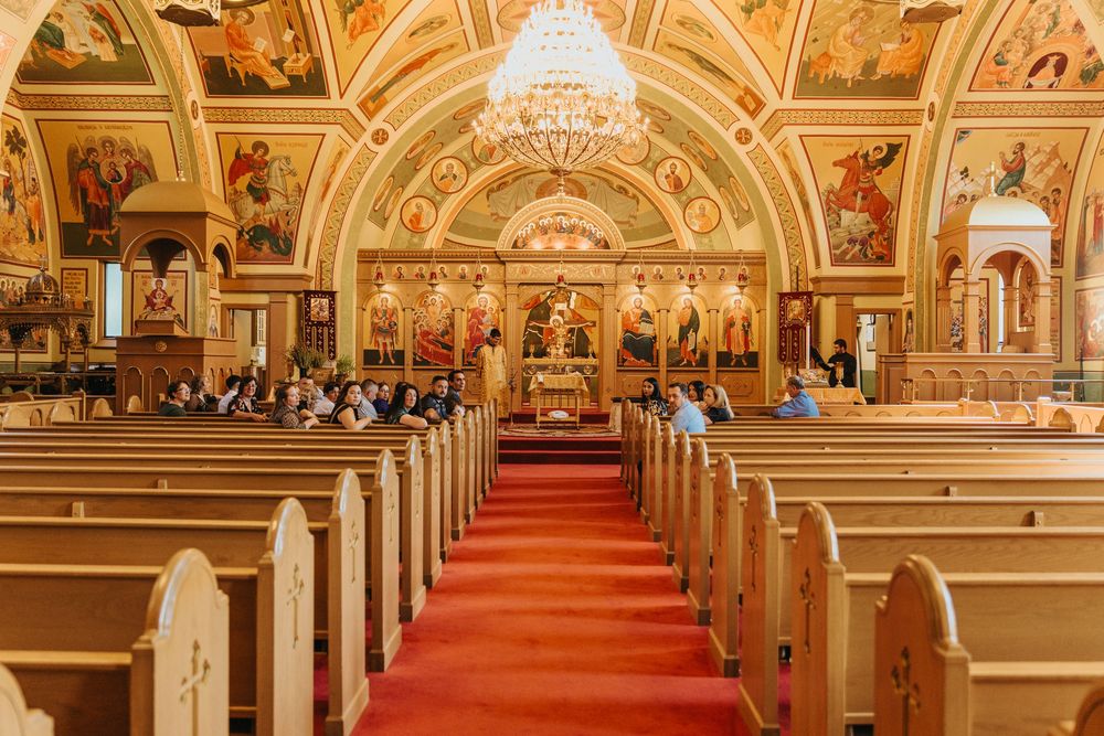 Interior of an ornate Catholic church with red carpet, wooden pews, and gold-painted baroque details on vaulted ceilings.