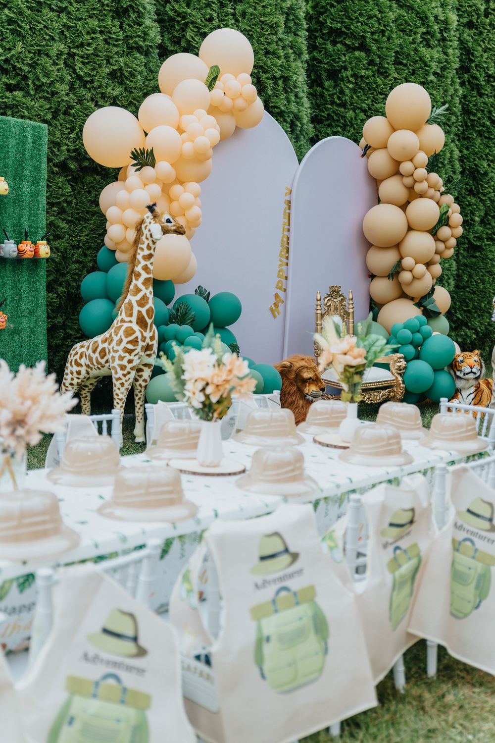 Safari themed party table with peach and teal balloon garland, giraffe decorations, and place settings on a white tablecloth.