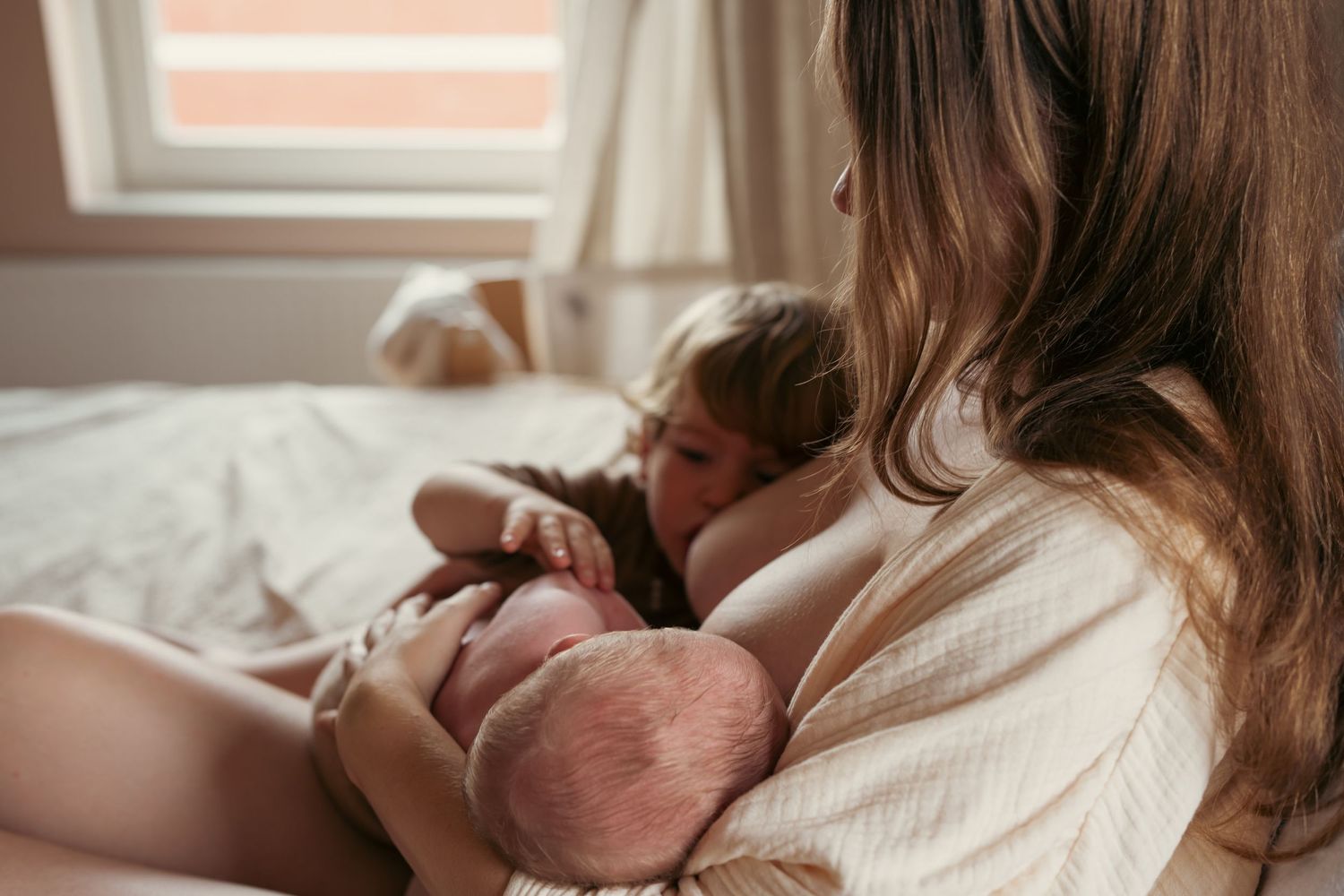 vrouw geeft borstvoeding aan haar twee kinderen tegelijk