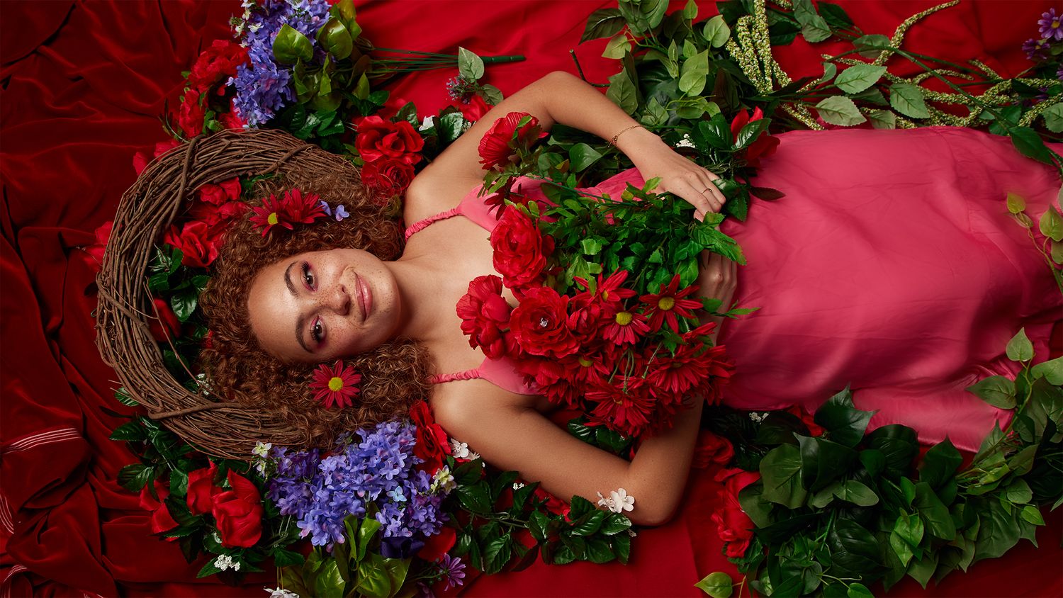 Artistic portrait with flowers and greenery on red velvet backdrop.