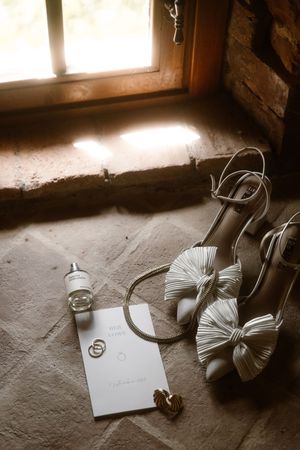 Sepia-toned sequence of wedding rings and shoes arranged near a window with natural light creating dramatic shadows.