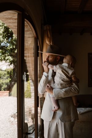 A tender moment captured in warm light through an arched doorway as a figure in beige holds a small child.