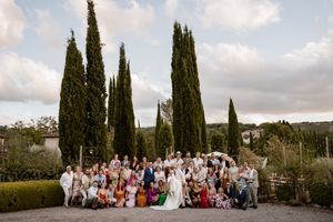A panoramic view of tall cypress trees lining a path under cloudy skies in a Mediterranean landscape.