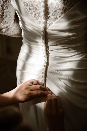 A series of detailed shots showing hands lacing up the back of an elegant white wedding dress with satin fabric.
