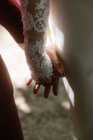 A close-up of two hands holding each other, with one arm wearing delicate white lace bridal sleeve detail.