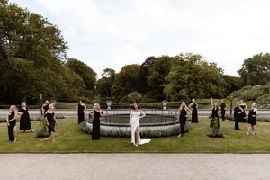 A group of people gather in a park setting for a wedding ceremony under large shade trees.