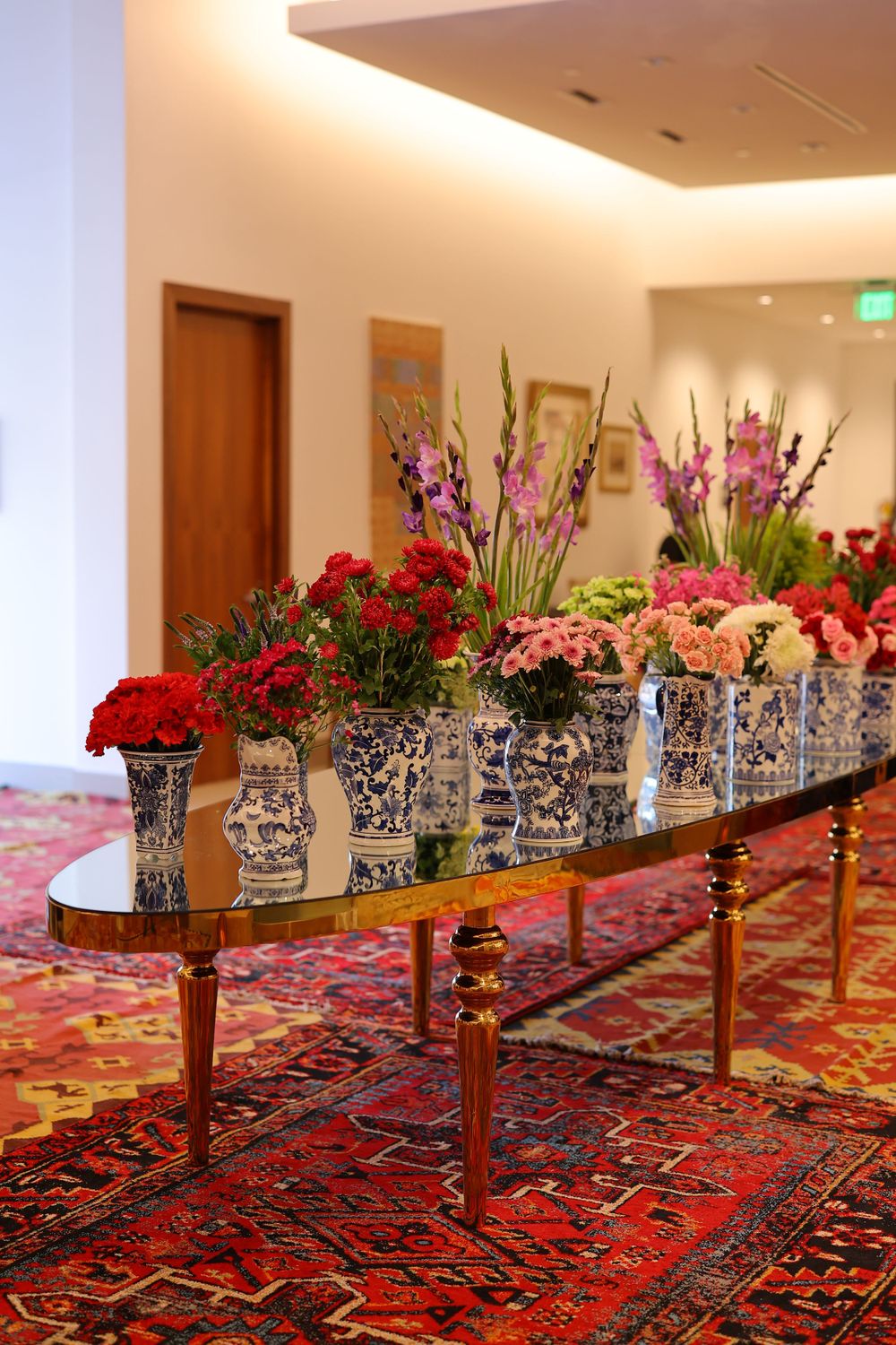 Elegant floral display with red and purple blooms in delft vases on an ornate table with Persian carpet.