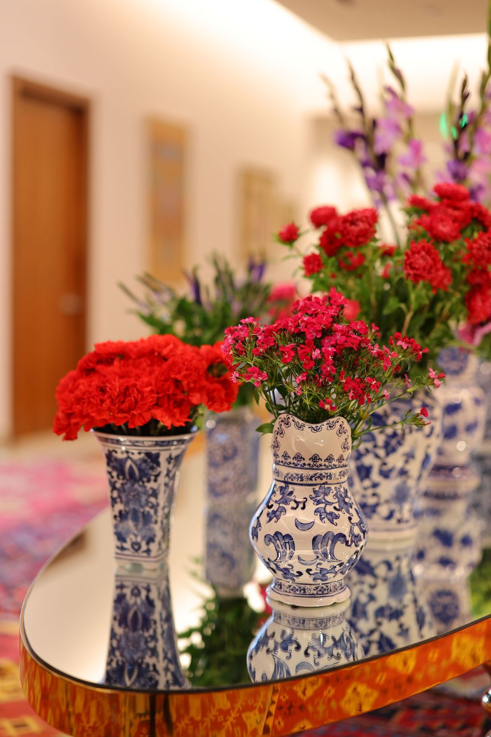 Beautiful red carnations and purple flowers arranged in blue and white porcelain vases on a mirrored table.