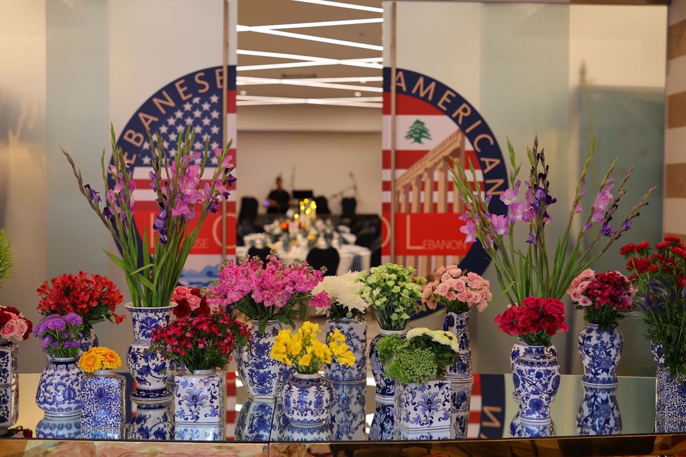Colorful flower arrangements in blue and white vases against backdrop of American and Lebanese flags.