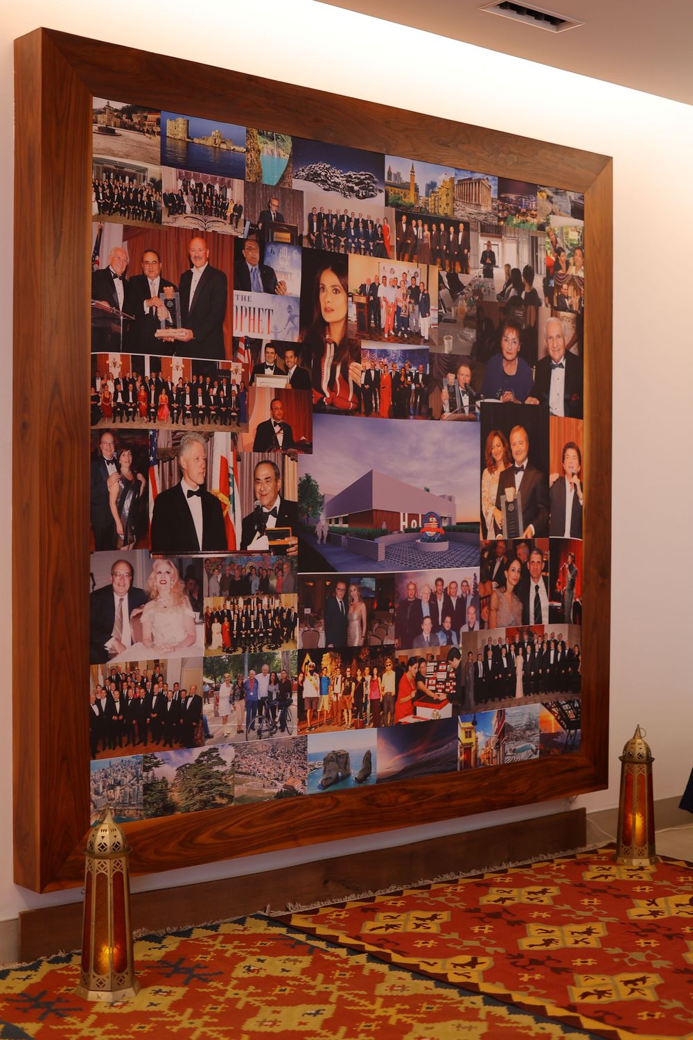 Large wooden-framed collage of event photos displayed on wall above ornate carpet.