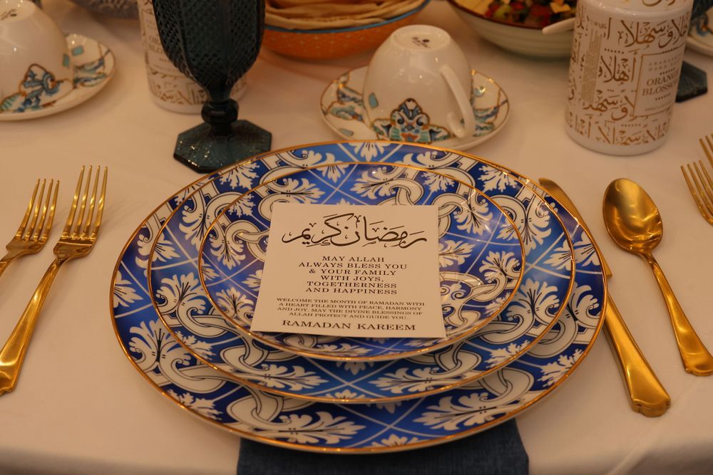 Elegant place setting with blue and white patterned plate, gold cutlery, and Arabic menu card.