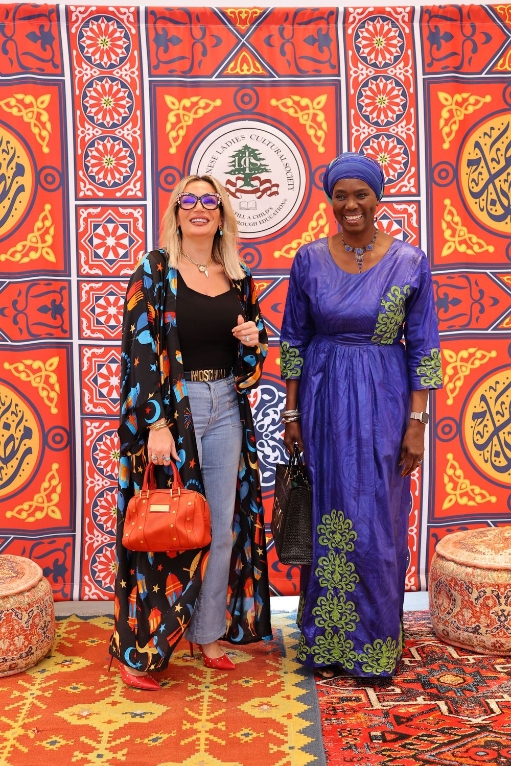 Two friends wearing contrasting outfits pose in front of ornate Middle Eastern wall decor.