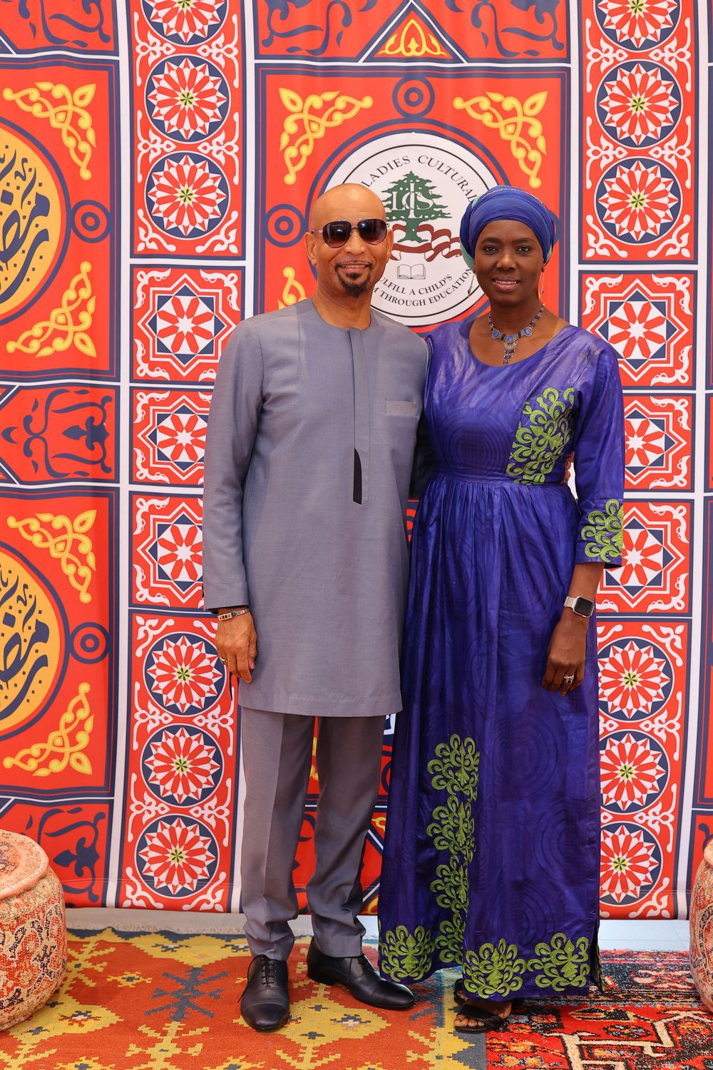Couple in formal attire poses against decorative Middle Eastern backdrop with geometric patterns.