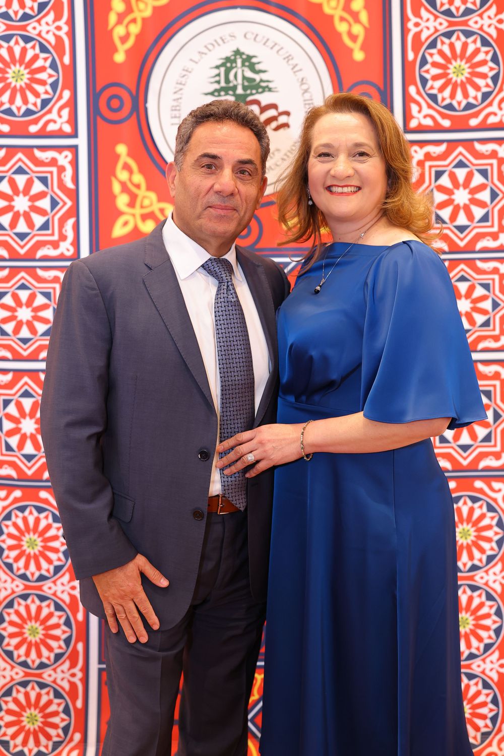 Couple in formal attire standing together against vibrant red and orange patterned background.