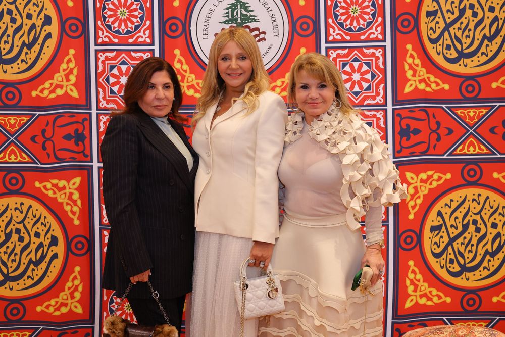 Three women in elegant evening wear pose against decorative Middle Eastern wall design.