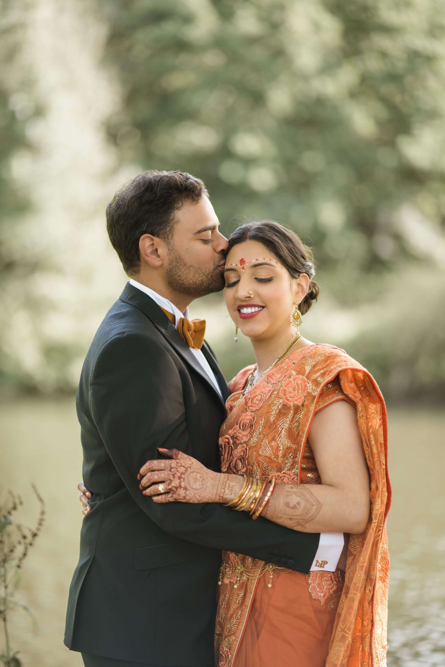 Groom is giving a kiss to his bride on the side of her forehead posing for the picture for the photographer.