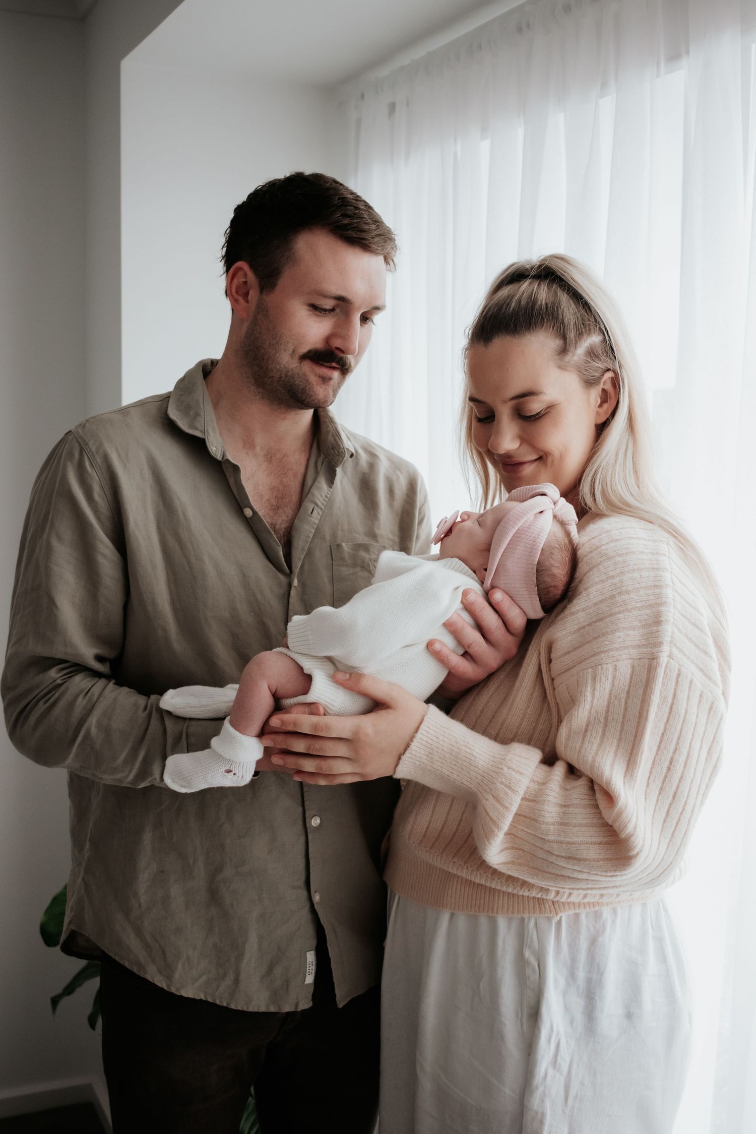 Mum and dad holding their newborn by the window.