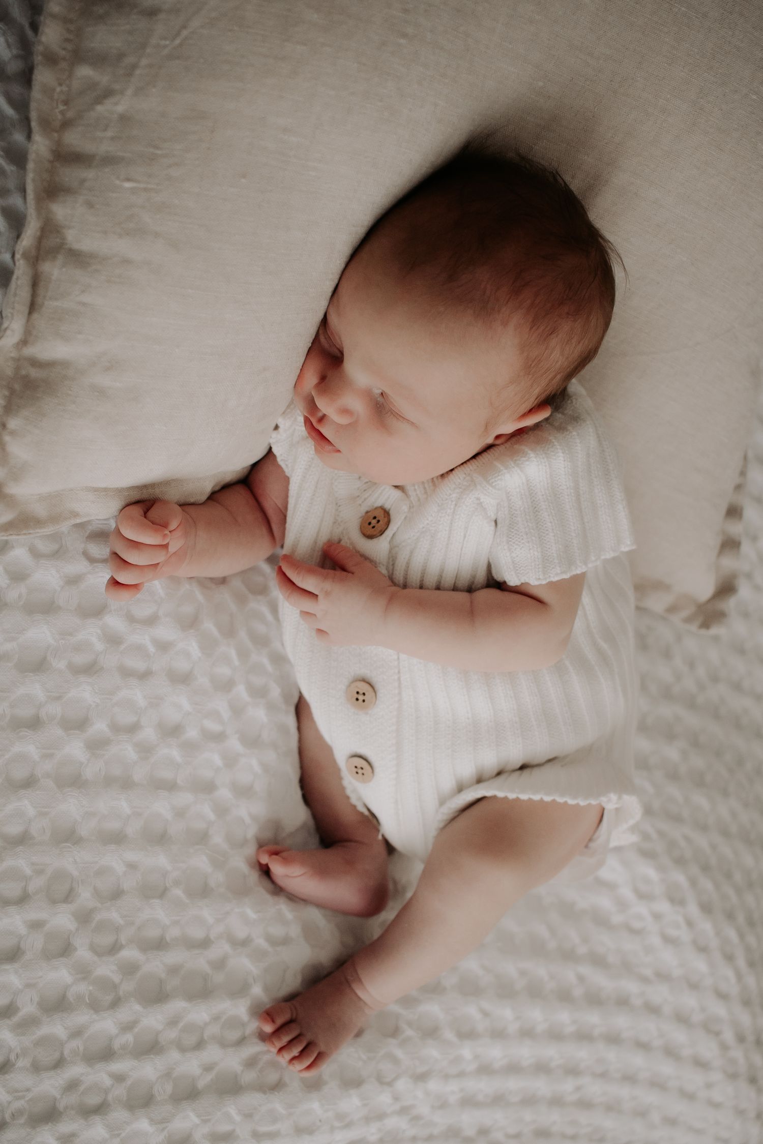 Baby asleep on a cushion on the bed.