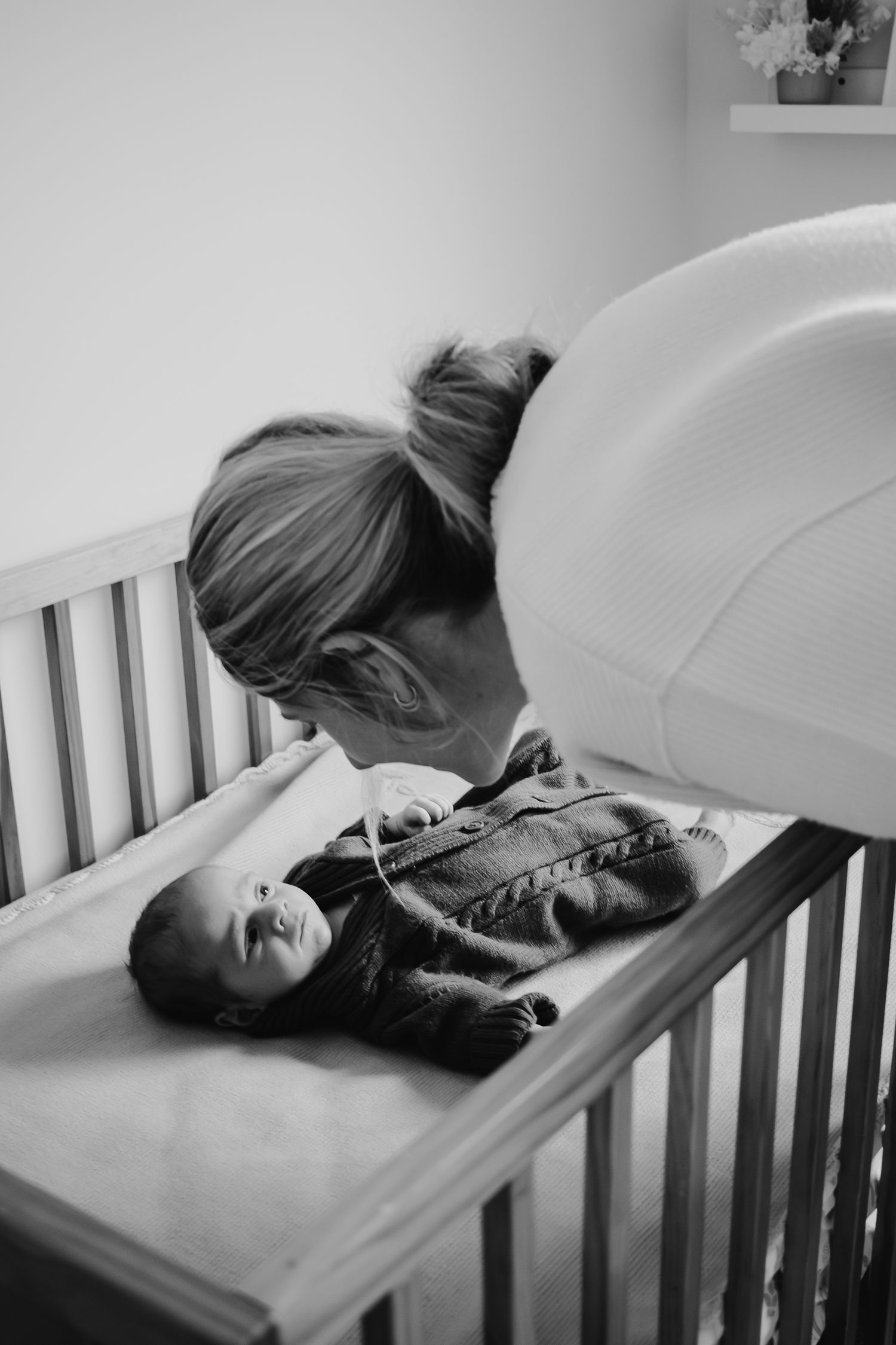 Mum looking down at baby in cot.