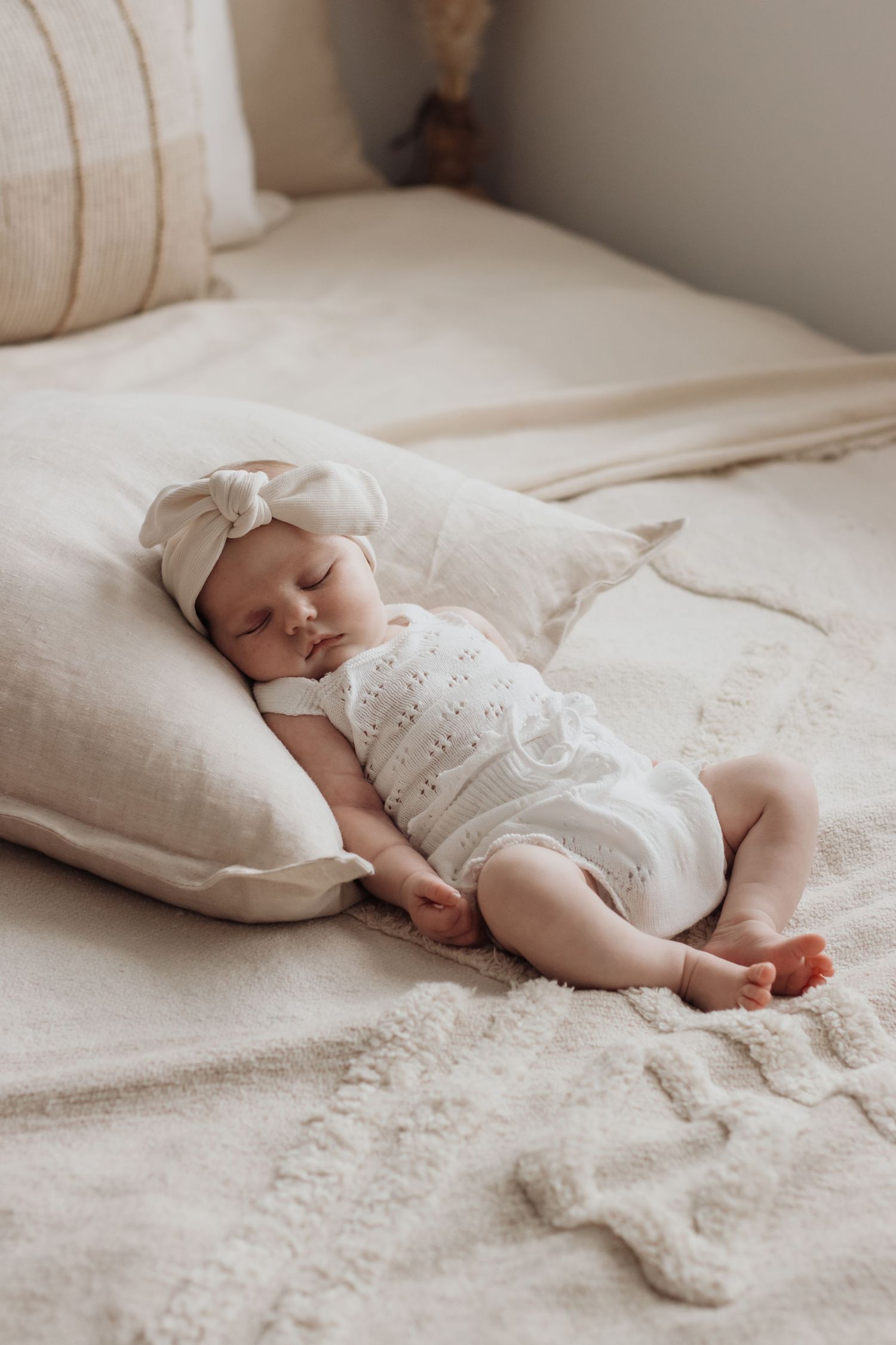 Baby asleep on a cushion on the bed.
