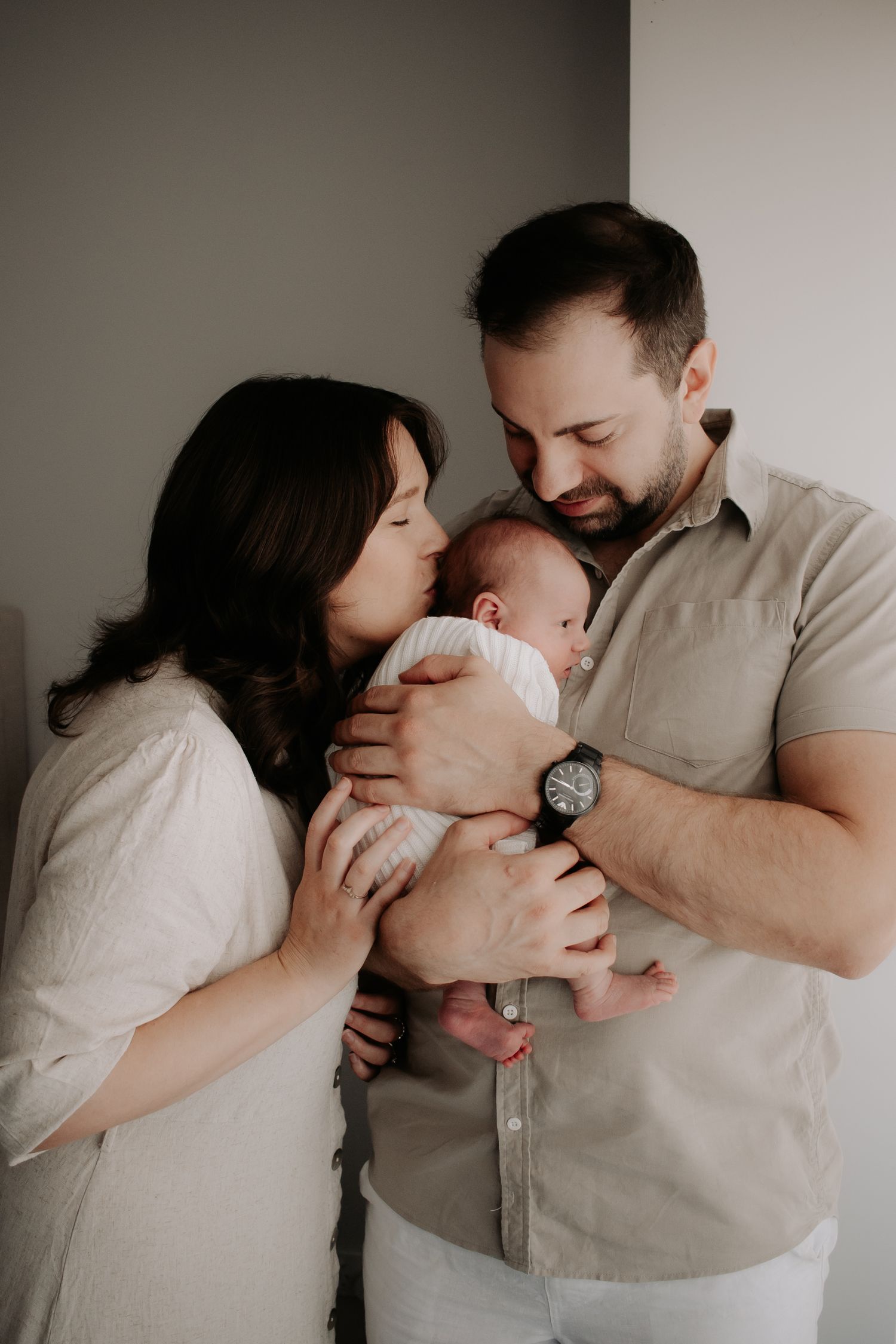 Mum and dad holding and kissing newborn baby's head.
