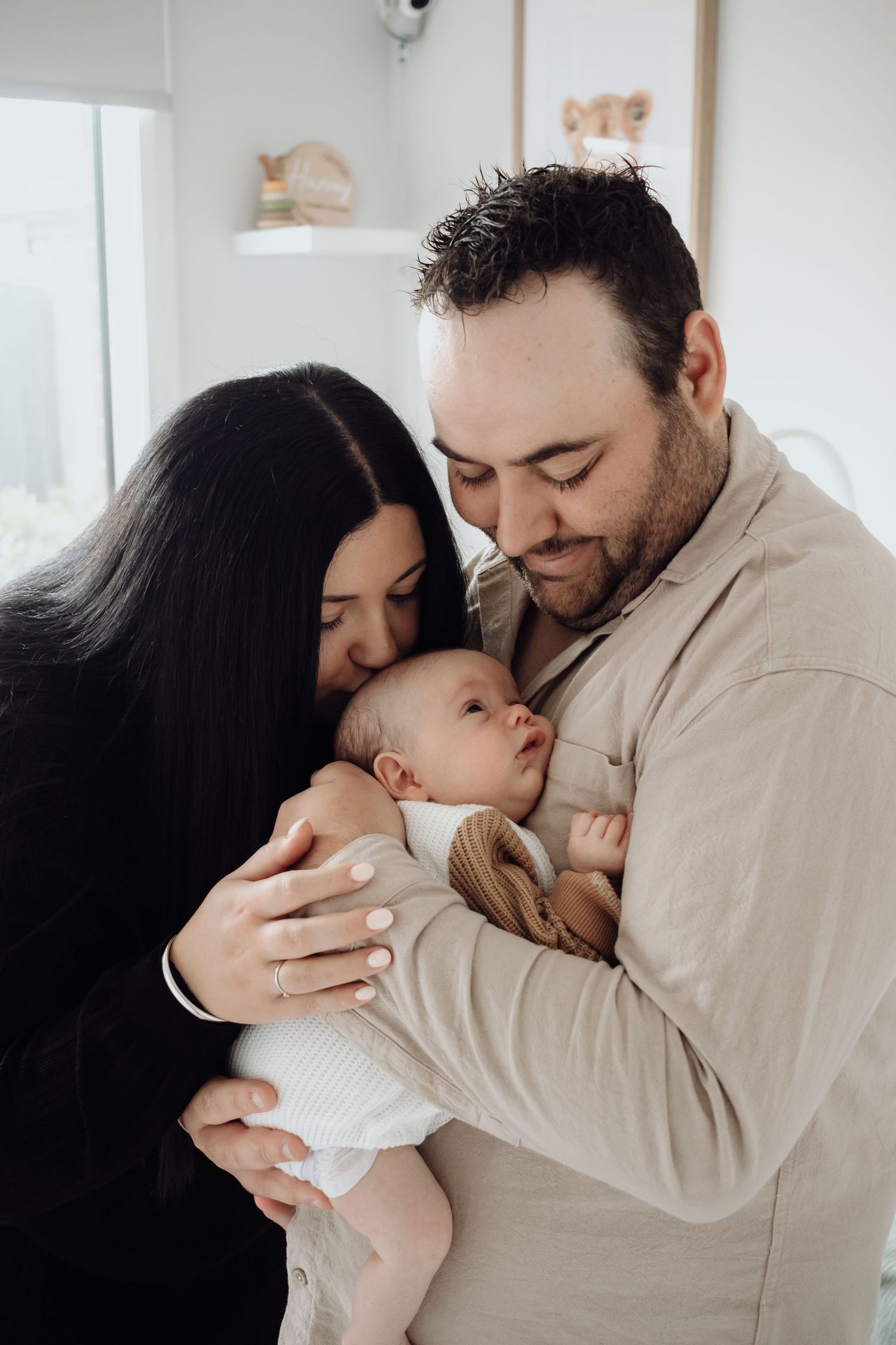 Dad holding baby while mum kisses their head.