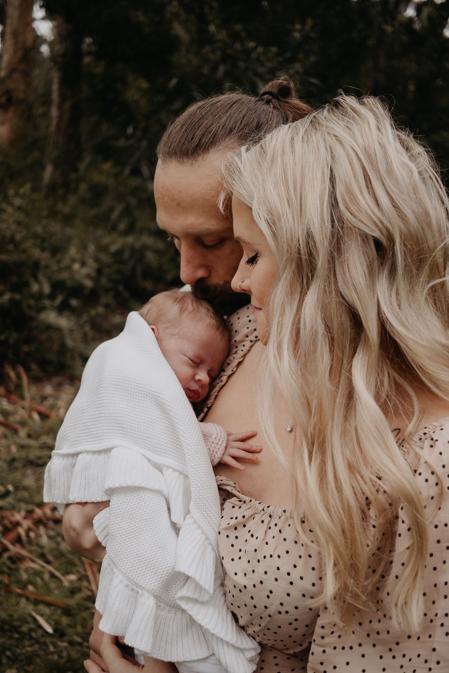 Mum holding baby while dad kisses newborn's head.