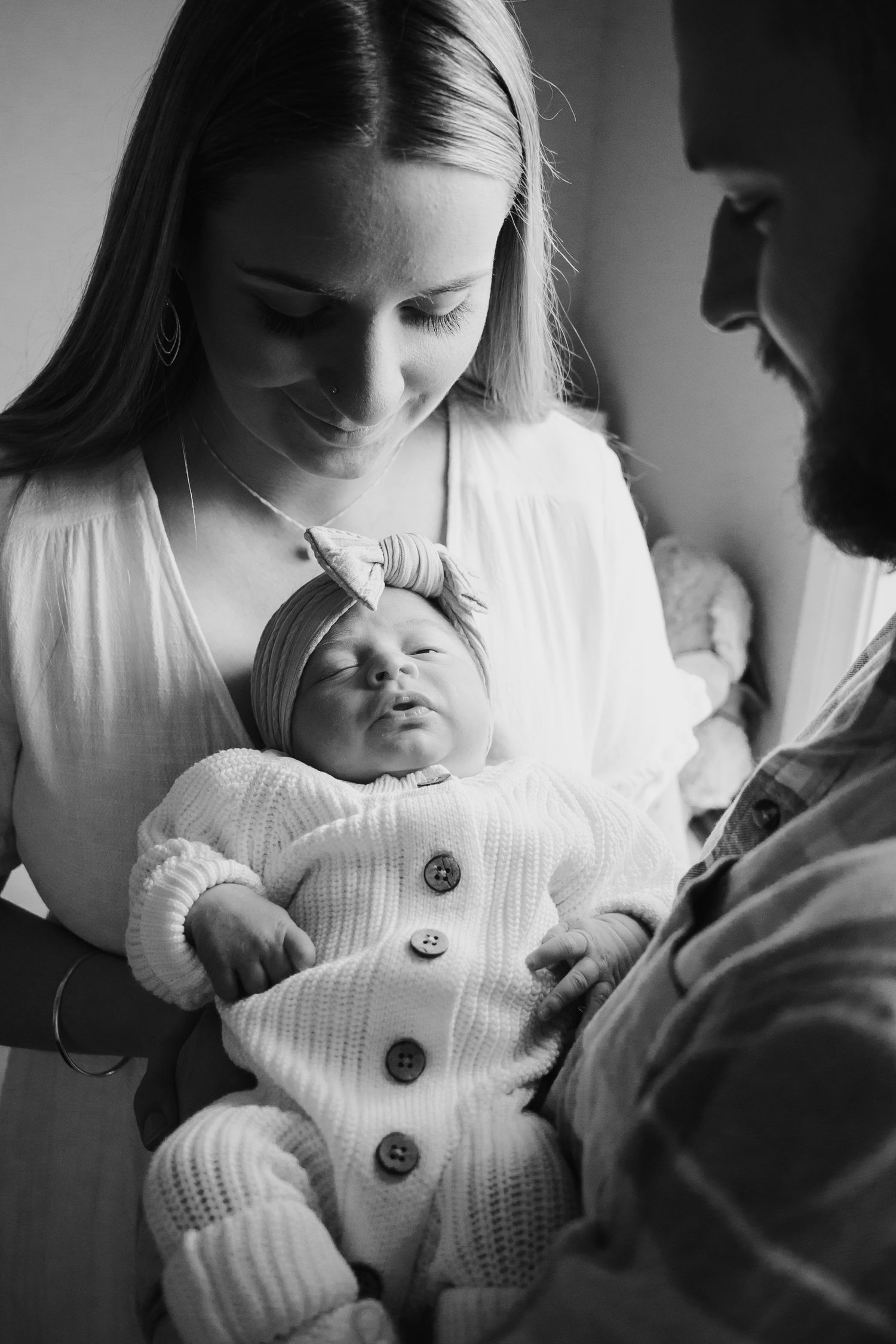 Mum and dad holding newborn while looking down at her.