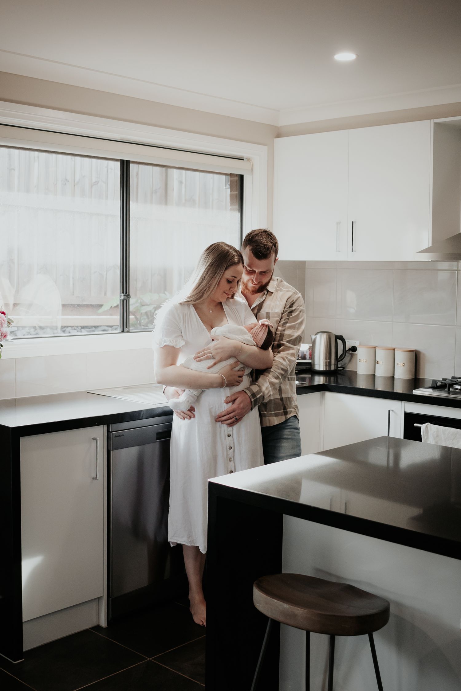 Mum and dad holding baby in their kitchen.