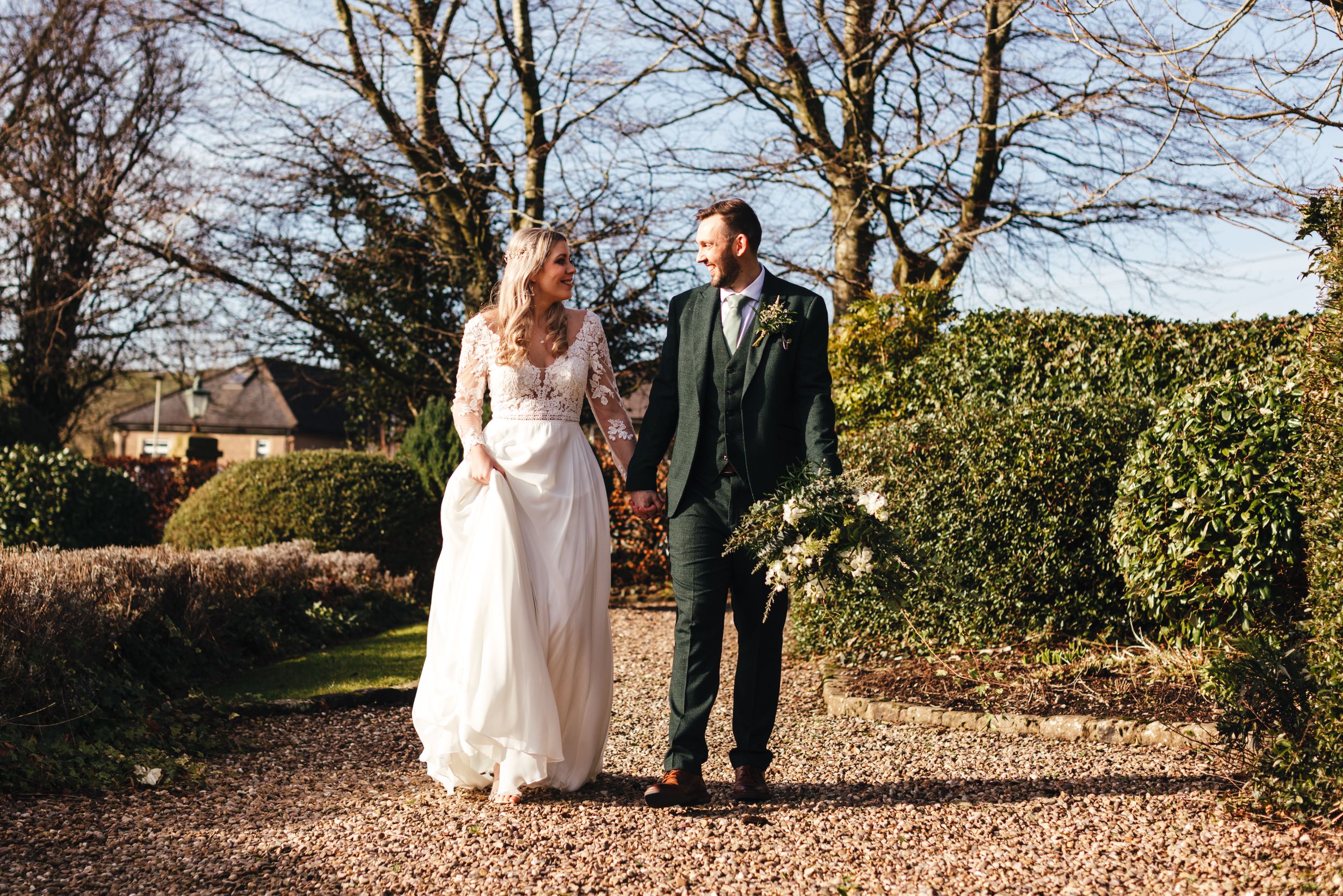 Couple walks hand in hand along gravel path surrounded by winter garden scenery.