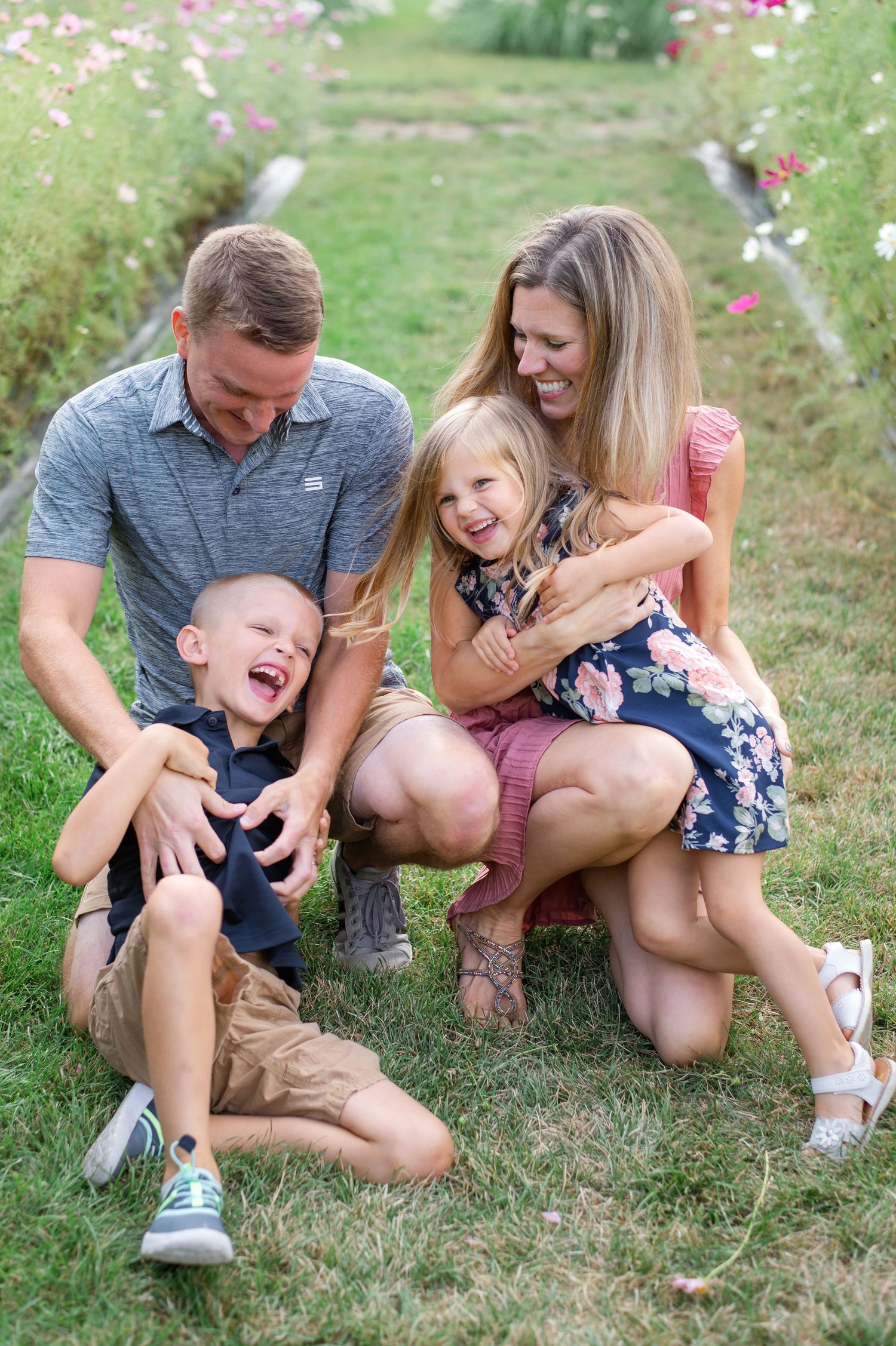 A family laughs together while sitting in a meadow with pink wildflowers.