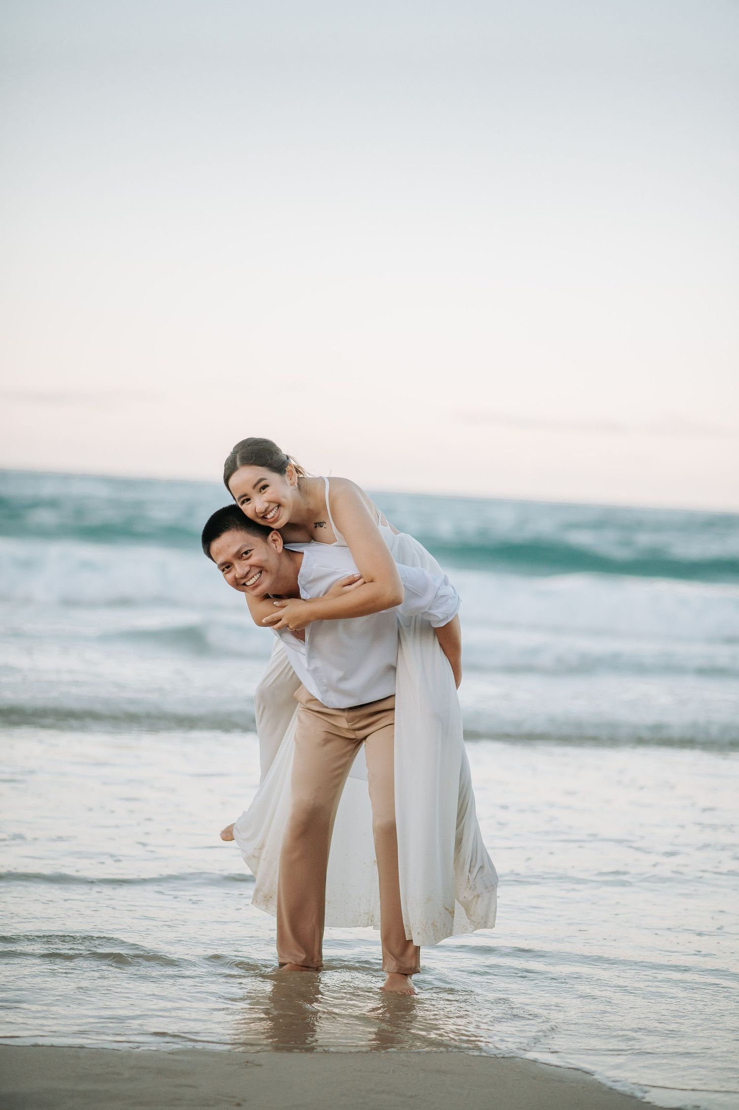 A playful moment between a couple in wedding attire at the beach during sunset.