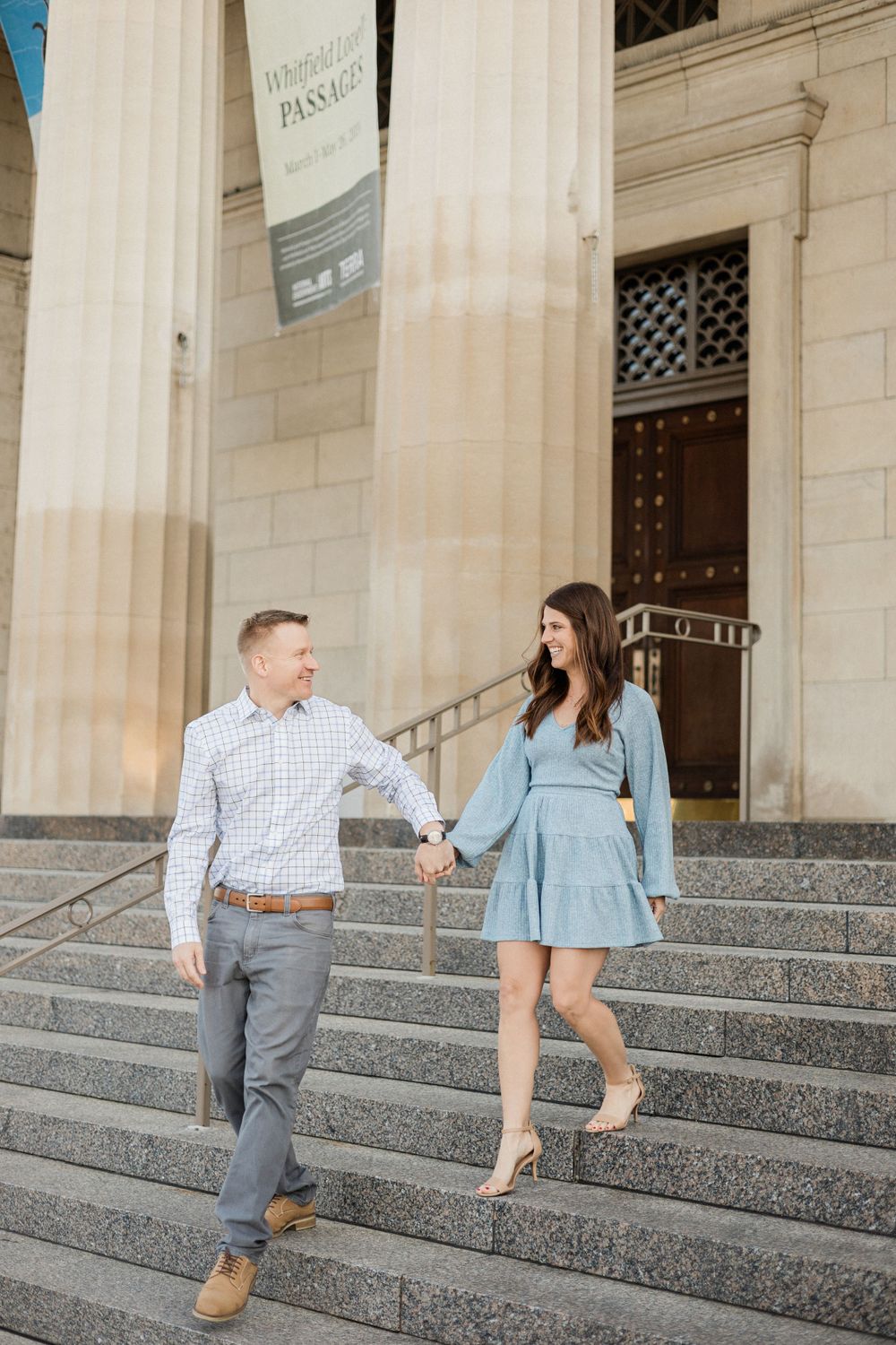 A couple walks down stone steps at Cincinnati Museum holding hands.