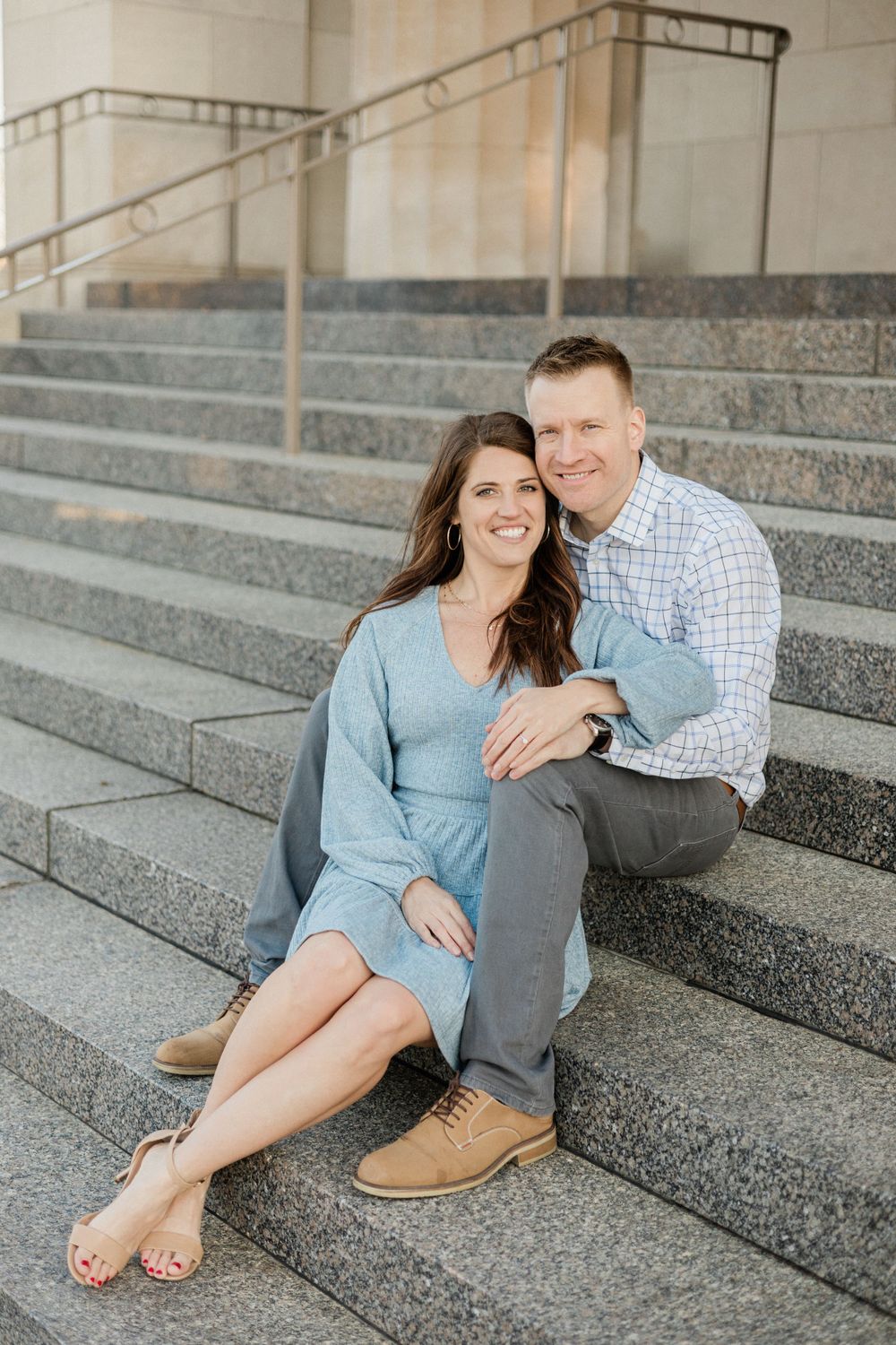 Couple shares an intimate moment sitting on grey stone steps of a building.